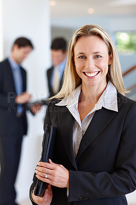 Buy stock photo Portrait of a female businesswoman standing indoors with two male colleagues behind her
