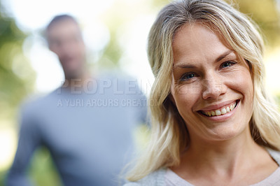 Buy stock photo Woman, portrait and smile outdoor with man in background by nature for park walk, happiness and date. Female person, happy and together as couple for love, romance and relax or mental health