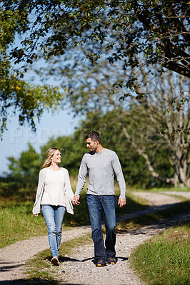 Buy stock photo Full length shot of a young couple walking hand in hand in a park