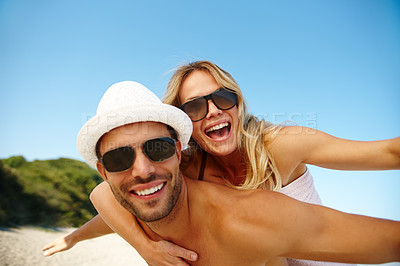 Buy stock photo Couple, sunglasses and piggyback on vacation, smile and peace at beach or game by blue sky. People, happy and tropical island for bonding on weekend, outdoor nature and love for marriage or romance