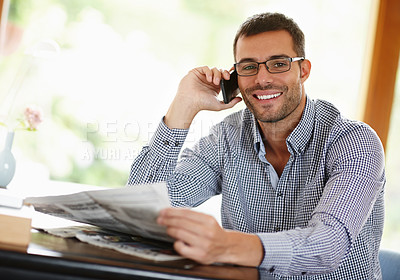Buy stock photo Portrait of a smiling young man reading the newspaper while on his mobile phone