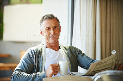 Buy stock photo A handsome mature man reading the newspaper while relaxing at home 