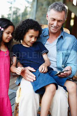 Buy stock photo Smile, bonding and man on sofa with smartphone, internet video or online movie. Grandkids, grandpa and technology for entertainment, sharing and comfort for family care visit together with children