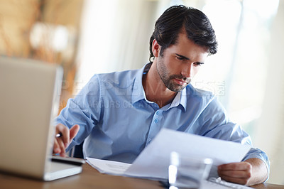 Buy stock photo A handsome young businessman working on his laptop at his desk