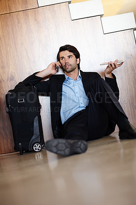 Buy stock photo A young businessman sitting on the floor and using his mobile while holding his tablet