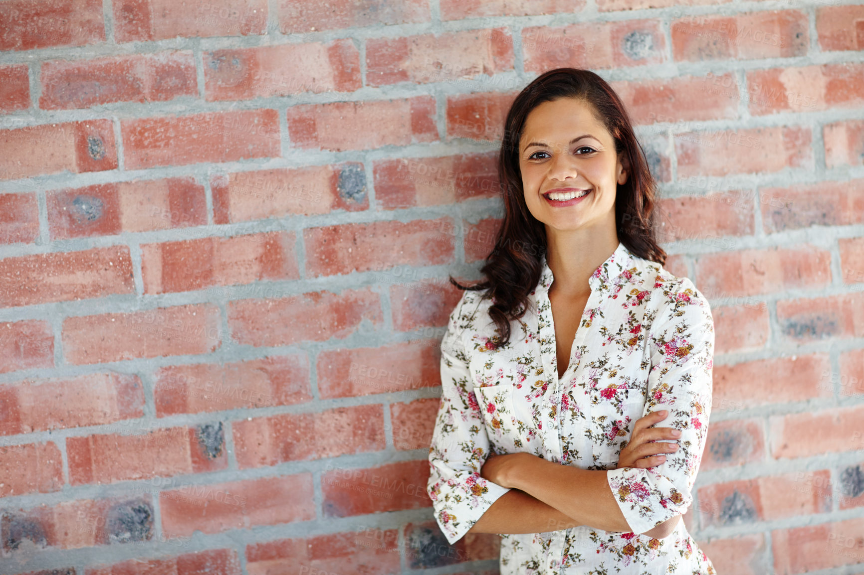 Buy stock photo An attractive young woman standing in front of a brick wall with her arms folded