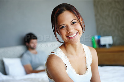 Buy stock photo Portrait of a smiling woman on the side of her bed with her boyfriend in the background