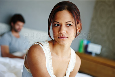 Buy stock photo Shot of an upset woman sitting on the side of her bed with her boyfriend in the background