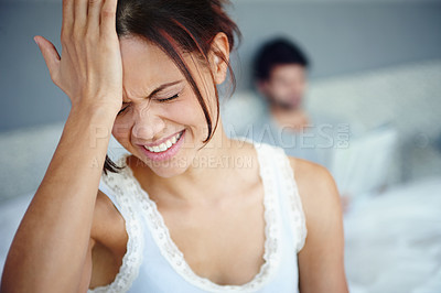 Buy stock photo Shot of a woman with her hand against her head sitting in her bedroom with her boyfriend in the background