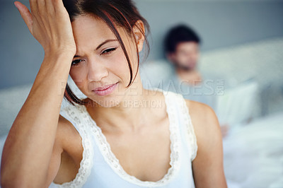 Buy stock photo Shot of a woman with her hand against her head sitting in her bedroom with her boyfriend in the background