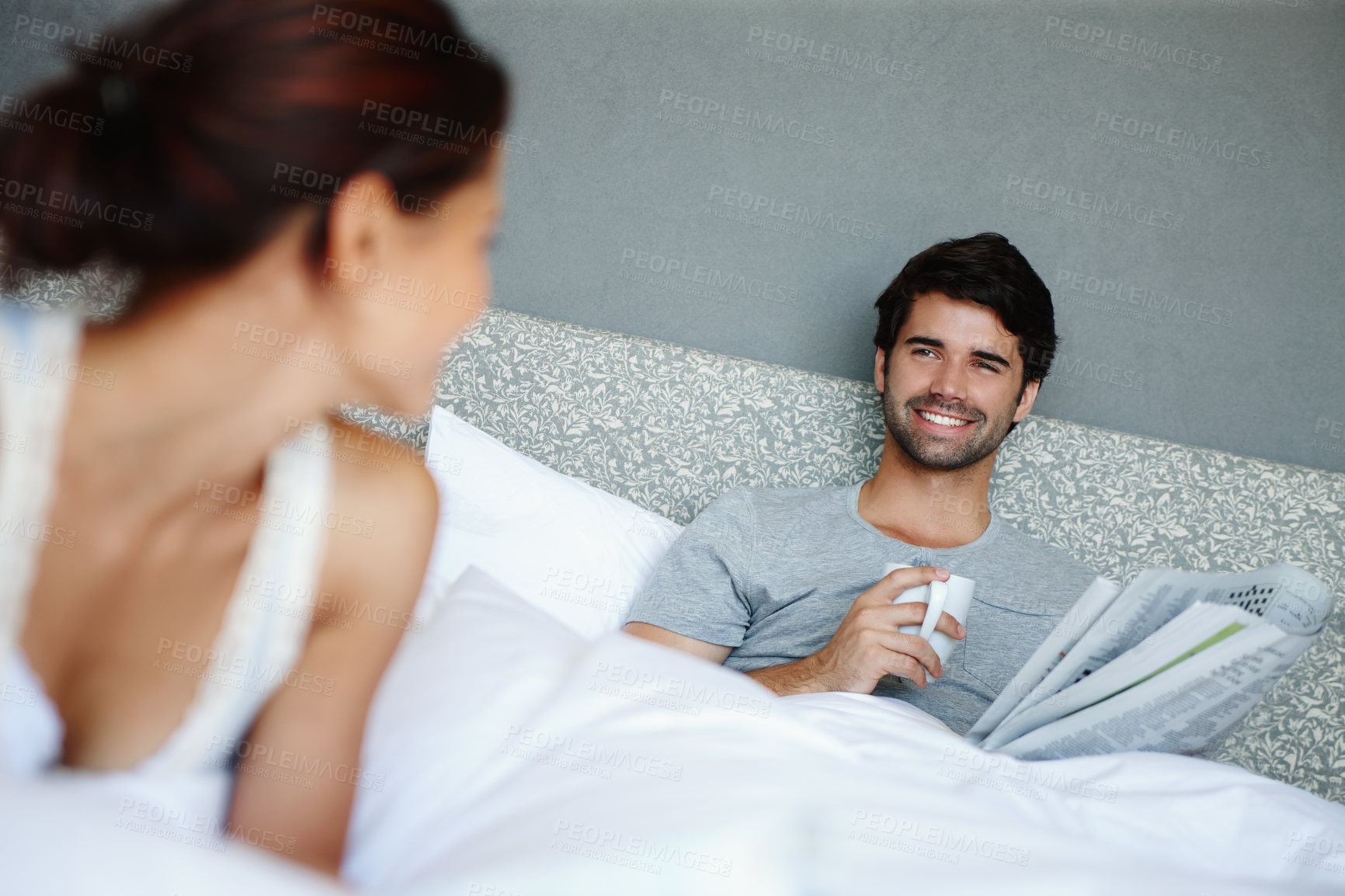 Buy stock photo Morning, woman and man in bedroom with coffee, newspaper and relax for bonding smile in home. Happy, face and couple in bed with romance, wellness and comfort in hotel room, house or apartment.