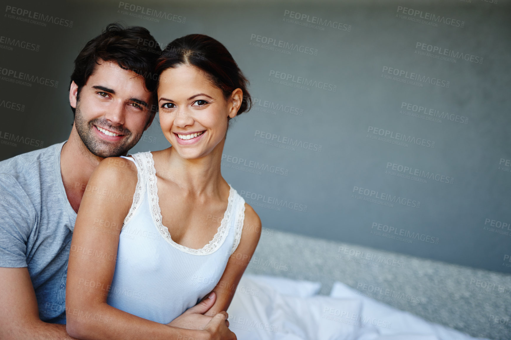 Buy stock photo Home, bed and couple in portrait with hug, bonding and comfortable together with smile. Young people, man and happy woman with love, romantic and commitment in marriage with mockup in apartment