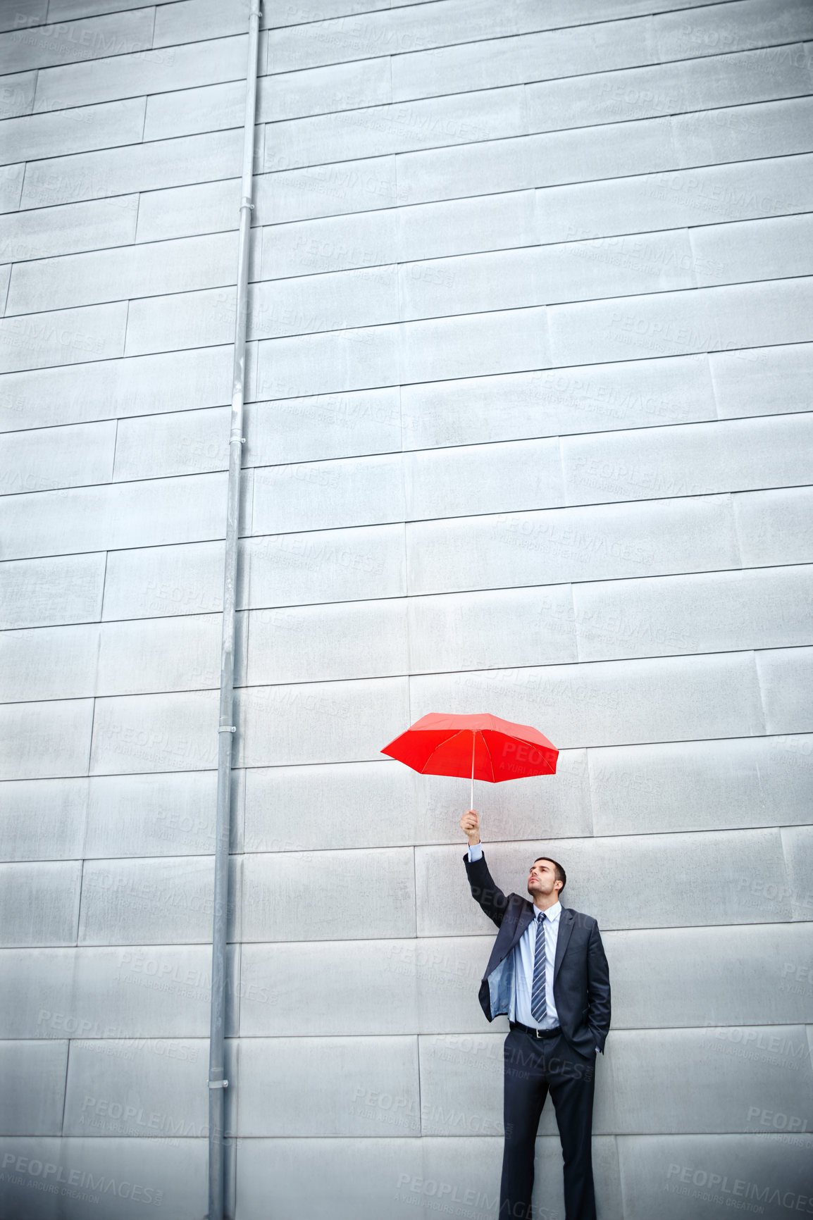 Buy stock photo A young businessman holding a red umbrella while outdoors