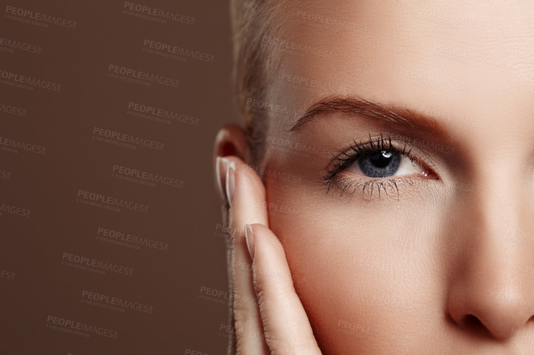 Buy stock photo Portrait of a beautiful woman's hand touching her face while wearing makeup, isolated on brown background. One female model with flawless, clear skin standing in a studio for beauty, skincare