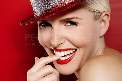 Buy stock photo Close up portrait of a beautiful showgirl biting her finger and smiling at the camera with a sparkly red hat on