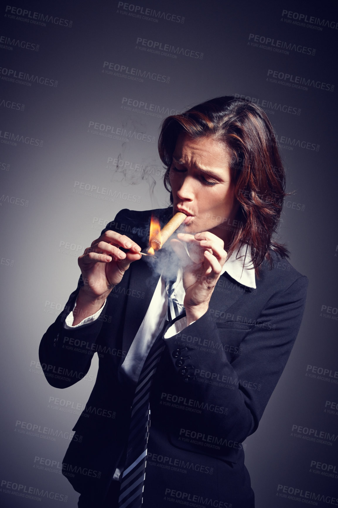 Buy stock photo A female mafia boss lighting a cuban cigar to celebrate success and increase in power. A beautiful successful entrepreneur wearing a tie and suit smoking a cigar against a black studio background