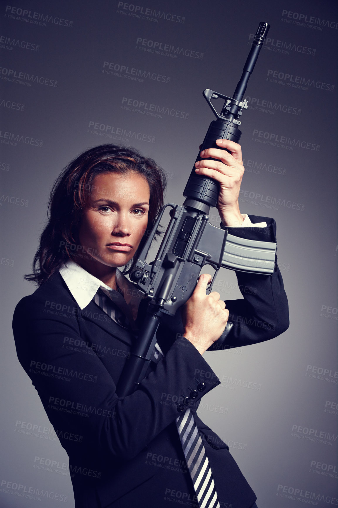 Buy stock photo A young businesswoman wearing a suit and tie holding a rifle