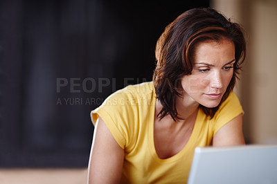 Buy stock photo Focused woman using a laptop to do freelance work while sitting at home. Female checking email or reading news online while using technology for telework business. Using the internet to work from home