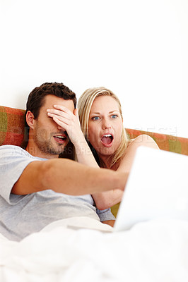 Buy stock photo A young couple lying in bed and using a laptop