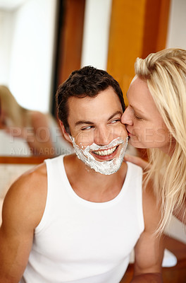 Buy stock photo A handsome man with shaving cream on his face smiling while his girlfriend kisses his cheek