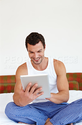 Buy stock photo A man sitting on his bed holding a digital tablet