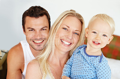 Buy stock photo Two parents smiiling at the camera with their young son while they sit on their bed