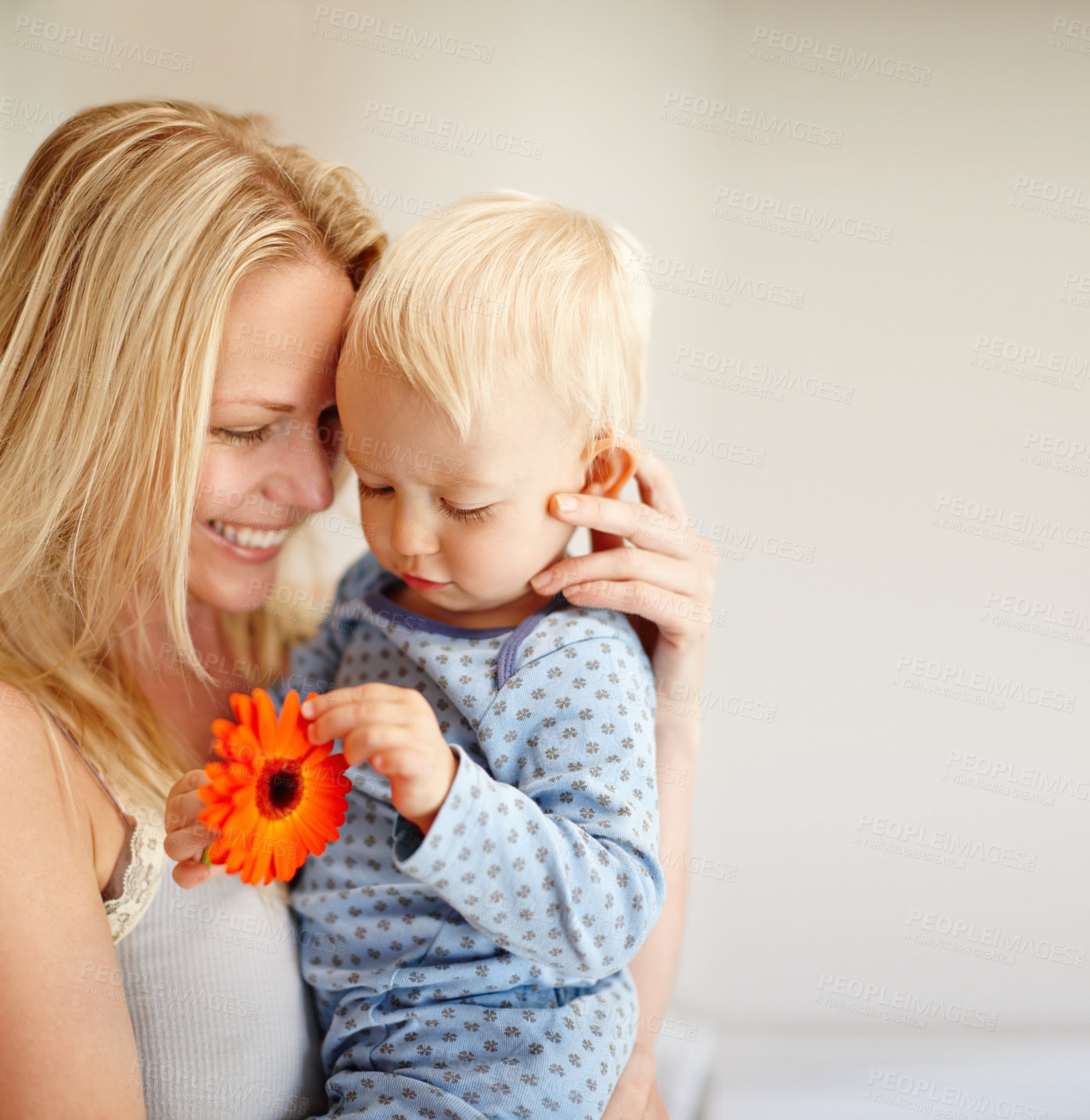 Buy stock photo A loving mother holding her son as he looks at an orange flower