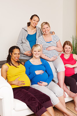 Buy stock photo A group of multi-ethnic pregnant women sitting on a couch and smiling at the camera