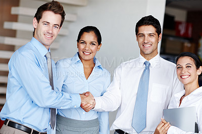 Buy stock photo Two businessmen sealing the deal with a handshake while their colleagues look on happily