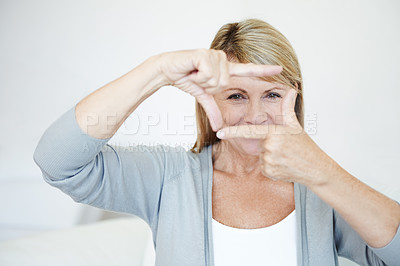 Buy stock photo Mature woman, portrait and fingers with frame for picture, moment or capture on sofa at home. Senior female person with gesture, eyes or face for photography, memory or sight in living room at house