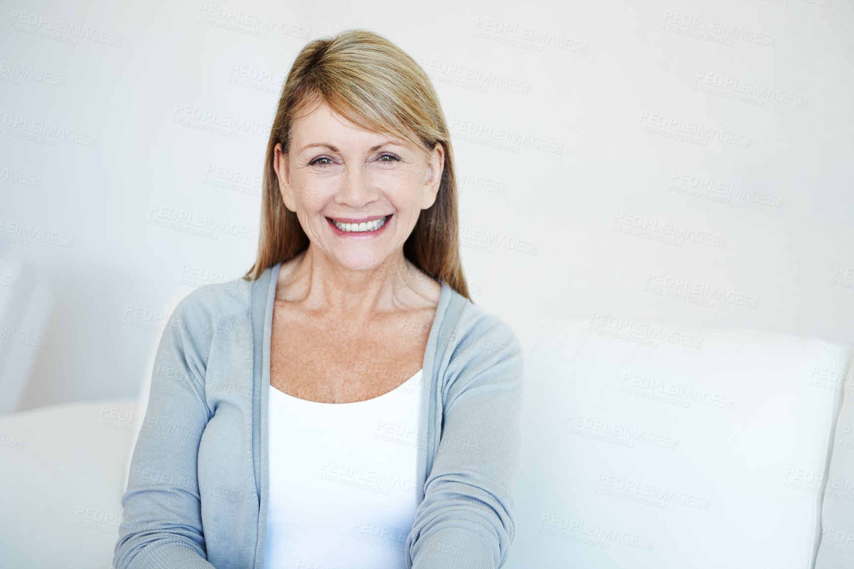 Buy stock photo Portrait of a smiling senior lady sitting in a white room with copy space. Elegant and kind mature woman relaxing on a couch at home. Older female enjoying her comfortable retirement inside