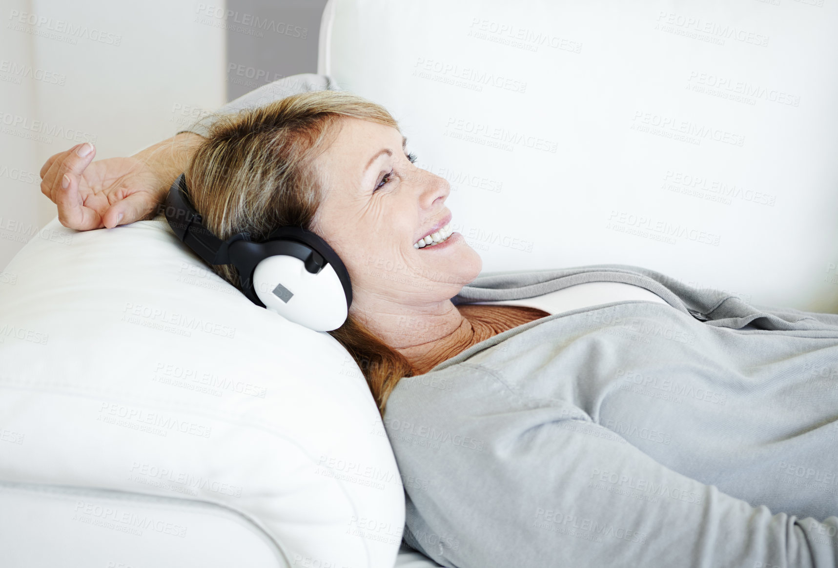 Buy stock photo Mature woman, headphones and relax on sofa in home, living room and smile for listening to radio. Person, music and subscription for audio book, happy and streaming with memory on couch in Germany