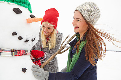 Buy stock photo Cropped shot of two beautiful young women building a snowman