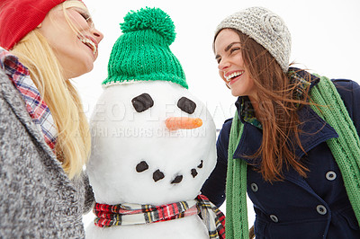 Buy stock photo Cropped shot of two beautiful young women standing beside a snowman