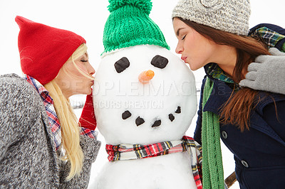 Buy stock photo Cropped shot of two beautiful young women kissing a snowman
