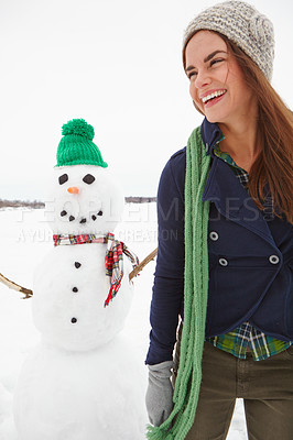 Buy stock photo Three quarter length shot of a young woman standing in front of a snowman