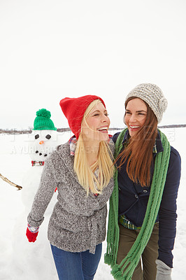 Buy stock photo Cropped shot of two young women walking passed a snowman