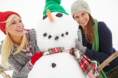 Buy stock photo Cropped shot of two gorgeous young women building a snowman