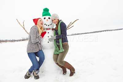Buy stock photo Cropped shot of two young woman having fun with a snowman