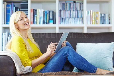 Buy stock photo Shot of a beautiful young woman sitting on the sofa and using a digtal tablet 