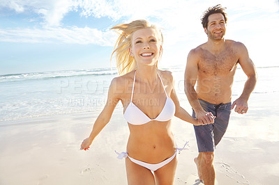 Buy stock photo Shot of a young couple running on a beach