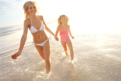 Buy stock photo Shot of a young mother and her daughter running through shallow water on the beach