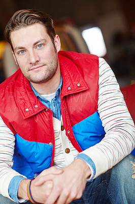 Buy stock photo Portrait of a trendy man in bright retro jacket sitting inside a fashion store. Young attractive male wearing casual stylish vintage red and blue color block vintage puffer with a stripe top