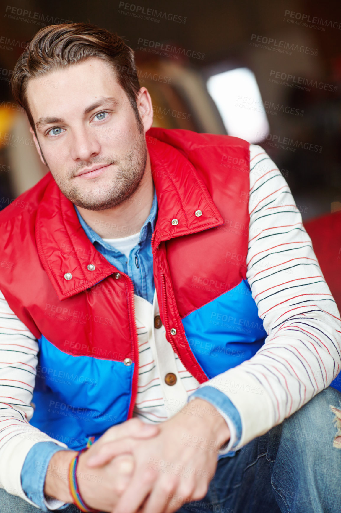 Buy stock photo Portrait of a trendy man in bright retro jacket sitting inside a fashion store. Young attractive male wearing casual stylish vintage red and blue color block vintage puffer with a stripe top