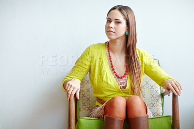Buy stock photo An attractive young woman wearing trendy clothes sitting comfortably on a chair indoors