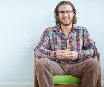 Buy stock photo A young man wearing a trendy plaid shirt sitting on an armchair indoors