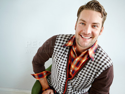 Buy stock photo A handsome young guy wearing a trendy outfit sitting on an armchair indoors and smiling looking happy sitting on a green chair. Portrait of a trendy guy in a cool outfit sitting on an armchair against a wall. Young smiling man in retro vintage stripe cardigan and casual shirt