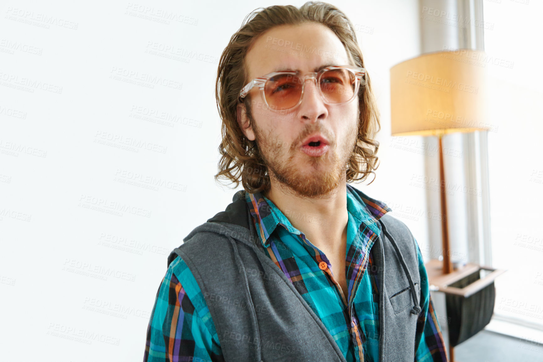 Buy stock photo A young man in a trendy outfit making a face while standing in a home interior