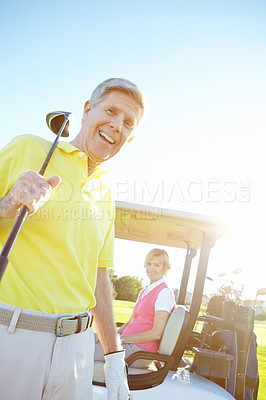 Buy stock photo Low angle shot of a handsome older golfer standing in front of a golf cart with his golfing buddy behind the wheel