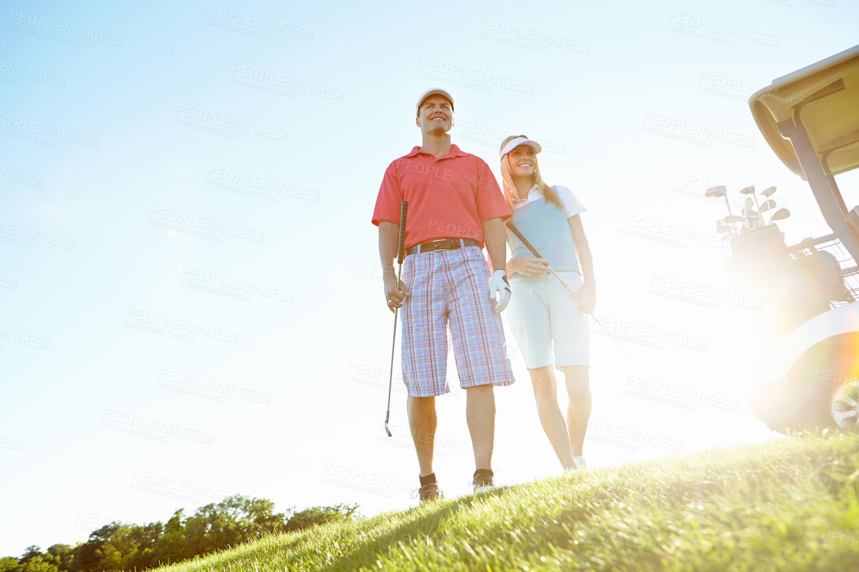 Buy stock photo Attractive golfing couple on the green with the sun setting behind them